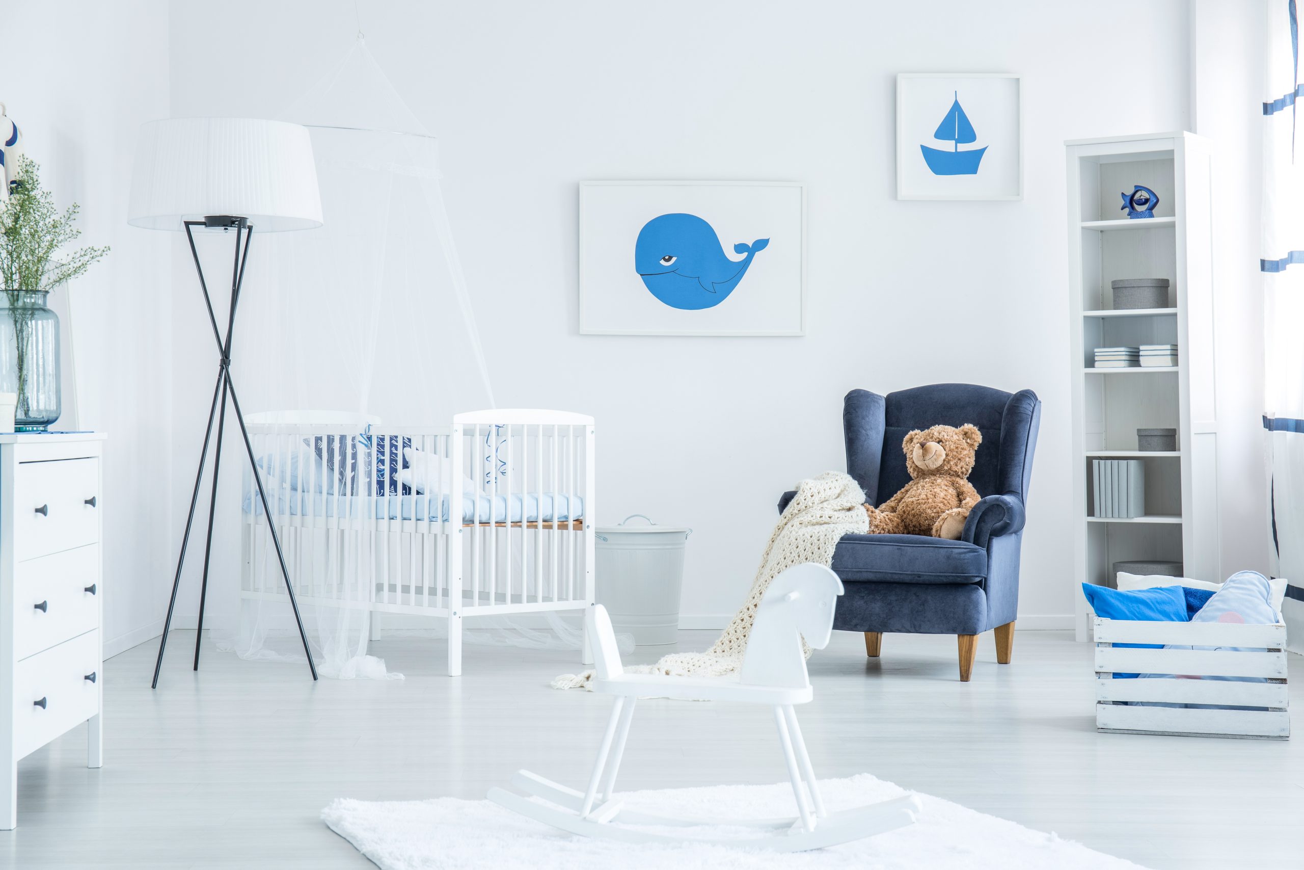 White rocking horse placed on the rug in simple baby room with dark armchair